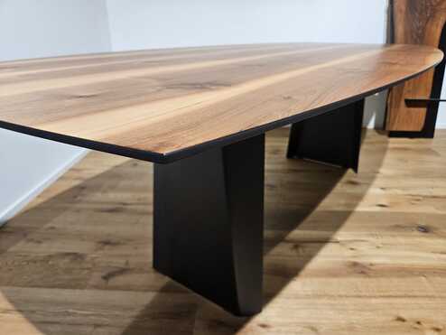 Eleganter Massivholztisch mit abgeschr&auml;gter Kante, nat&uuml;rlicher Holzmaserung und schwarzen Metallf&uuml;ssen auf einem Holzboden.