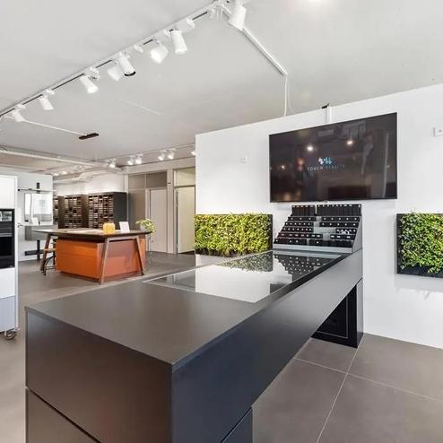 Küchenstudio mit modernen Ausstellungselementen Küchenstudio mit schwarzen Küchenmöbeln, Begrünungselementen, Musterpräsentationen und einem interaktiven Bildschirm für die Küchenplanung.