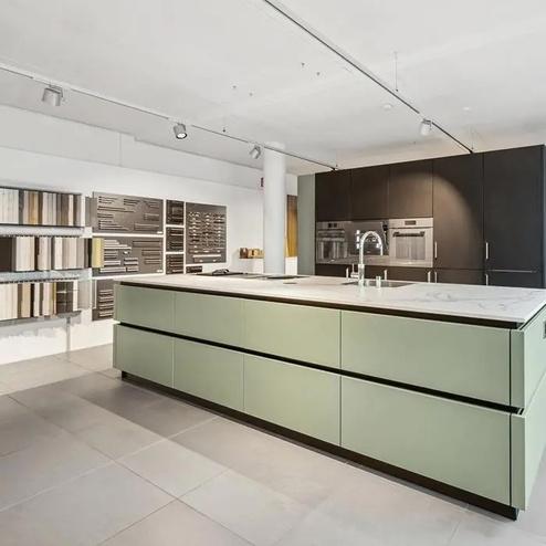 Moderne Designküche mit grüner Insel und dunklen Schränken Küche mit grosszügiger grüner Kücheninsel, Marmorarbeitsplatte, dunklen Einbauschränken und ausgestellten Materialmustern im Hintergrund.