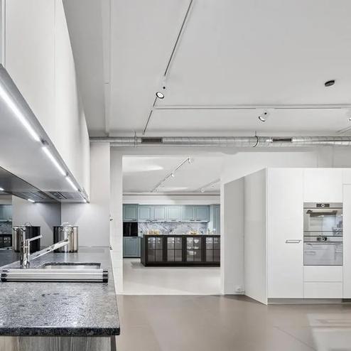 Küchenstudio mit modernen und klassischen Designelementen Küchenstudio mit weissen Hochglanzschränken, dunkler Arbeitsplatte und klassisch inspiriertem Küchenbereich in Blau- und Schwarztönen im Hintergrund.