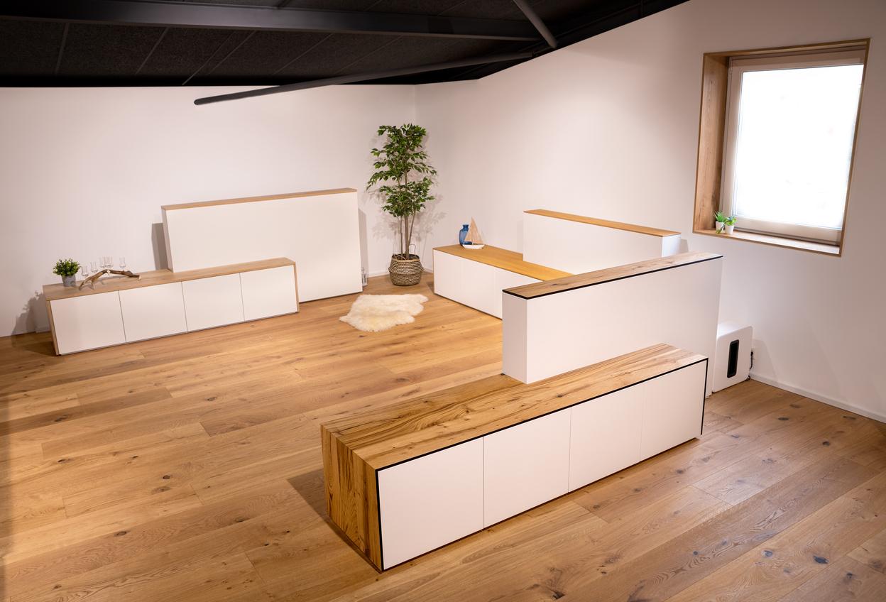 Mehrere weiße Sideboards mit Holzoberfläche und integriertem TV-Lift in modernem Showroom.