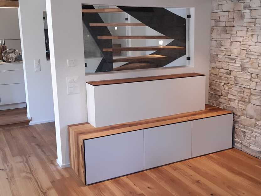 Modernes motorisiertes Fernsehm&ouml;bel mit Holz- und Weissdesign, erg&auml;nzt durch eine stilvolle Steinwand und Blick auf eine offene Treppe.