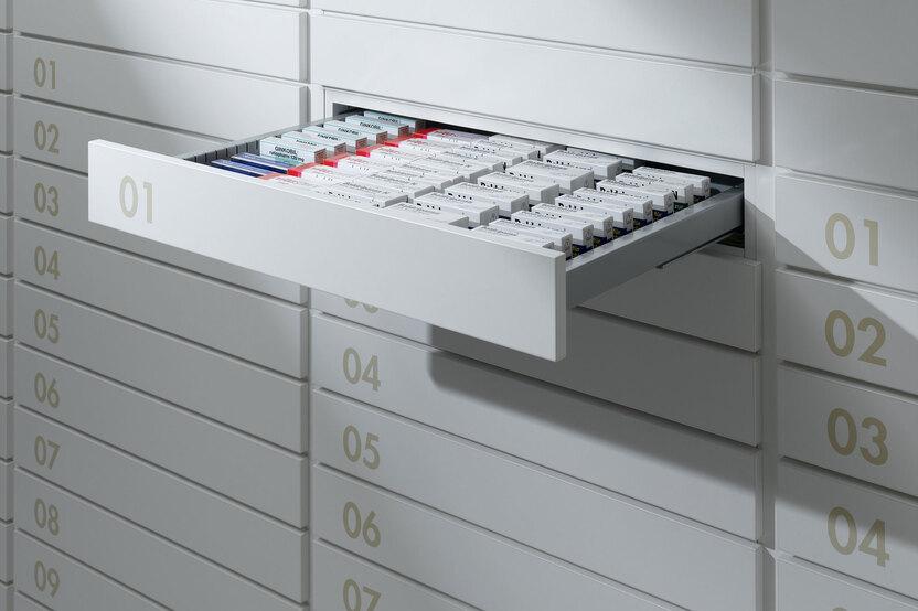 Detailaufnahme von schmalen weissen Medikamentenschubläden mit dezenter Nummerierung und sichtbarer Medikamentenaufteilungen.