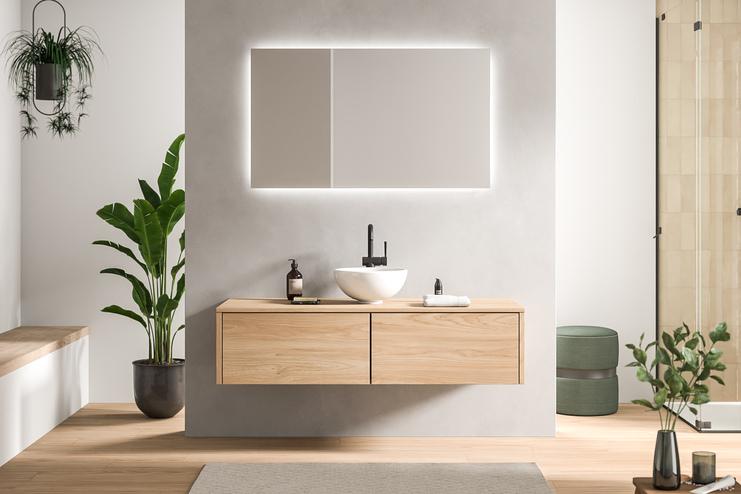 Geschmackvoll gestaltetes Bad nach Mass mit einem hellen Holzwaschtisch und einem rechteckigen, beleuchteten Spiegel, umgeben von Pflanzen.