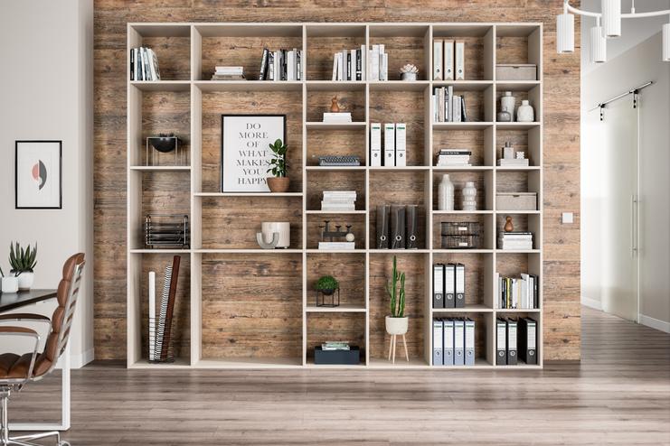 Ein grosses, helles Regal nach Mass, gefüllt mit Büchern und Dekorationen, vor einer Wand mit Holzoptik.