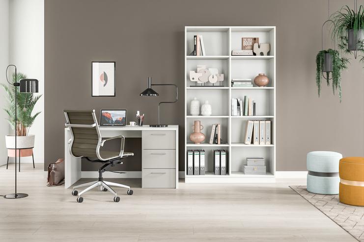 Helles Zimmer mit massgefertigtem, weissem Regal voller Bücher und Deko, Schreibtisch mit Computer, Pflanzen und Stühlen.