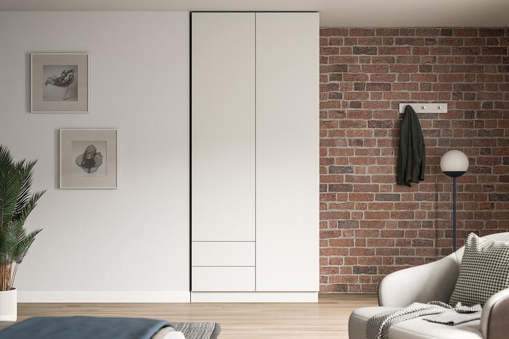 Eleganter Schrank nach Mass in modernem Wohnambiente Grosser, massgeschneiderter weisser Schrank im Kontrast zu einer Ziegelwand, neben Kunstwerken und einer stilvollen Stehlampe.