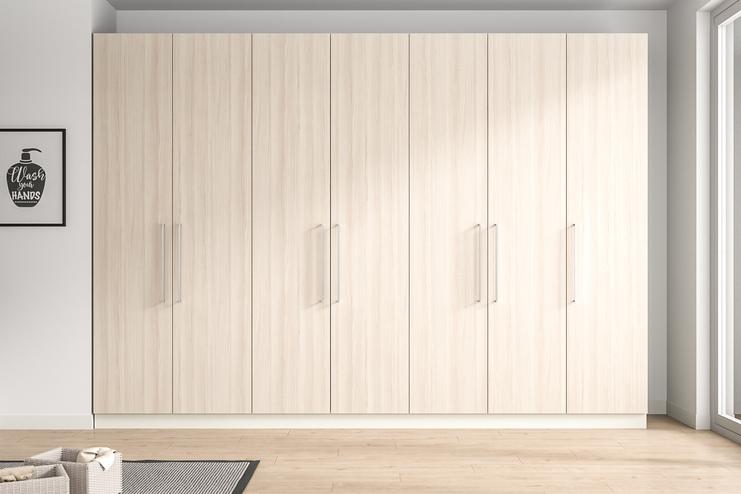 Grosser, massgefertigter Schrank in einem eleganten Zimmer. Wandfüllender, massgeschneiderter Schrank in heller Holzoptik mit minimalistischen Griffen, der nahtlos in das moderne Raumdesign integriert ist.