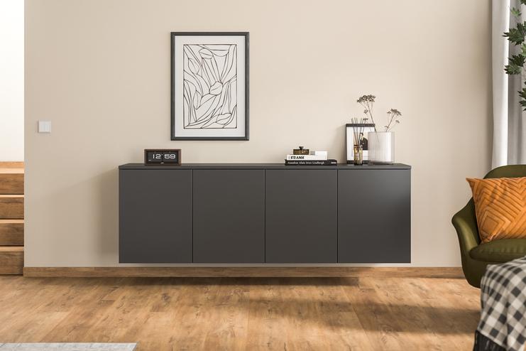 Ein massgeschneidertes Hängeboard in Anthrazit ergänzt den Wohnraum, stilvoll unter einem abstrakten Gemälde und neben einer grünen Samtsessel platziert.